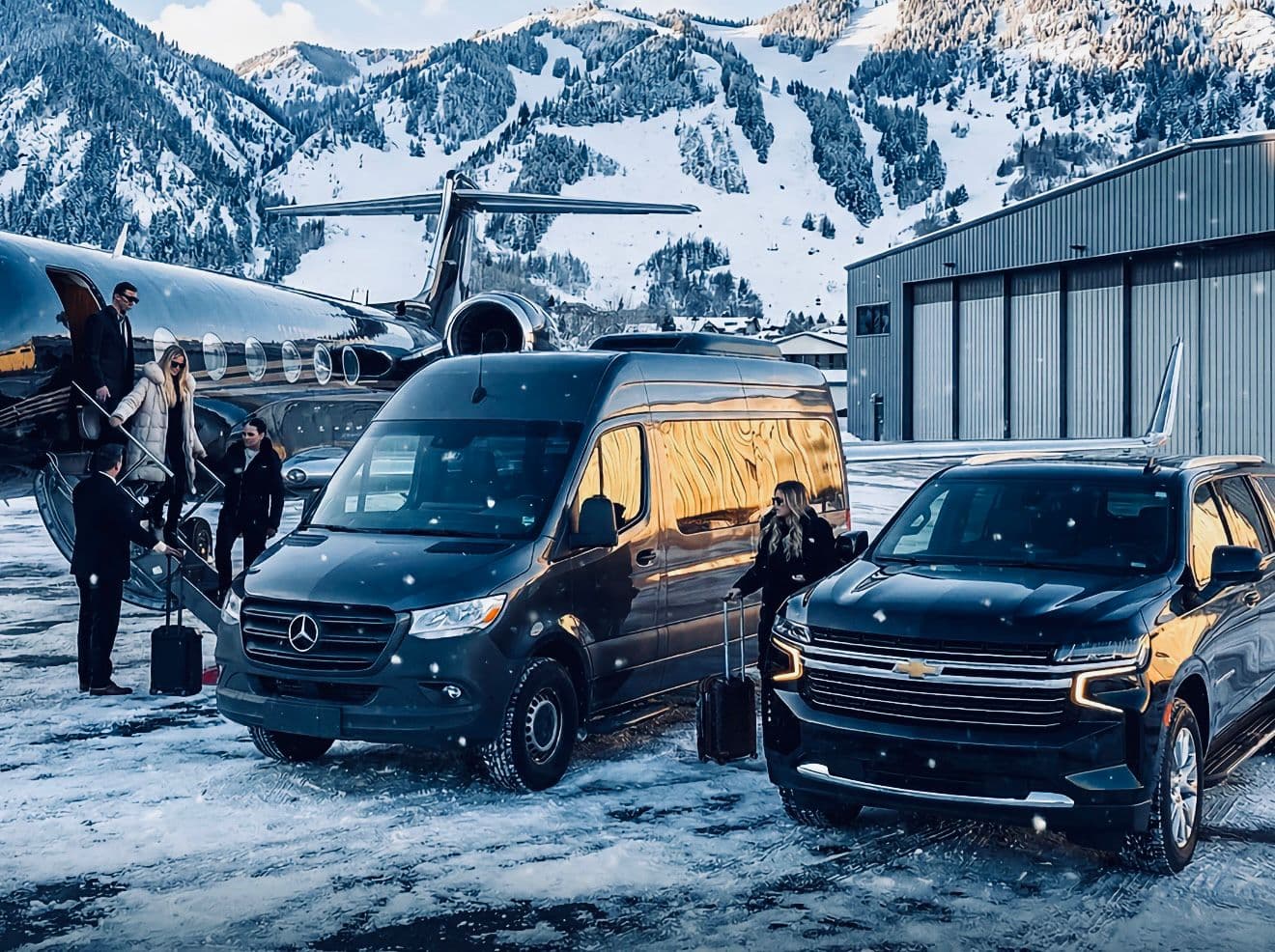 Black luxury van and SUV at private jet terminal with snow-capped mountains
